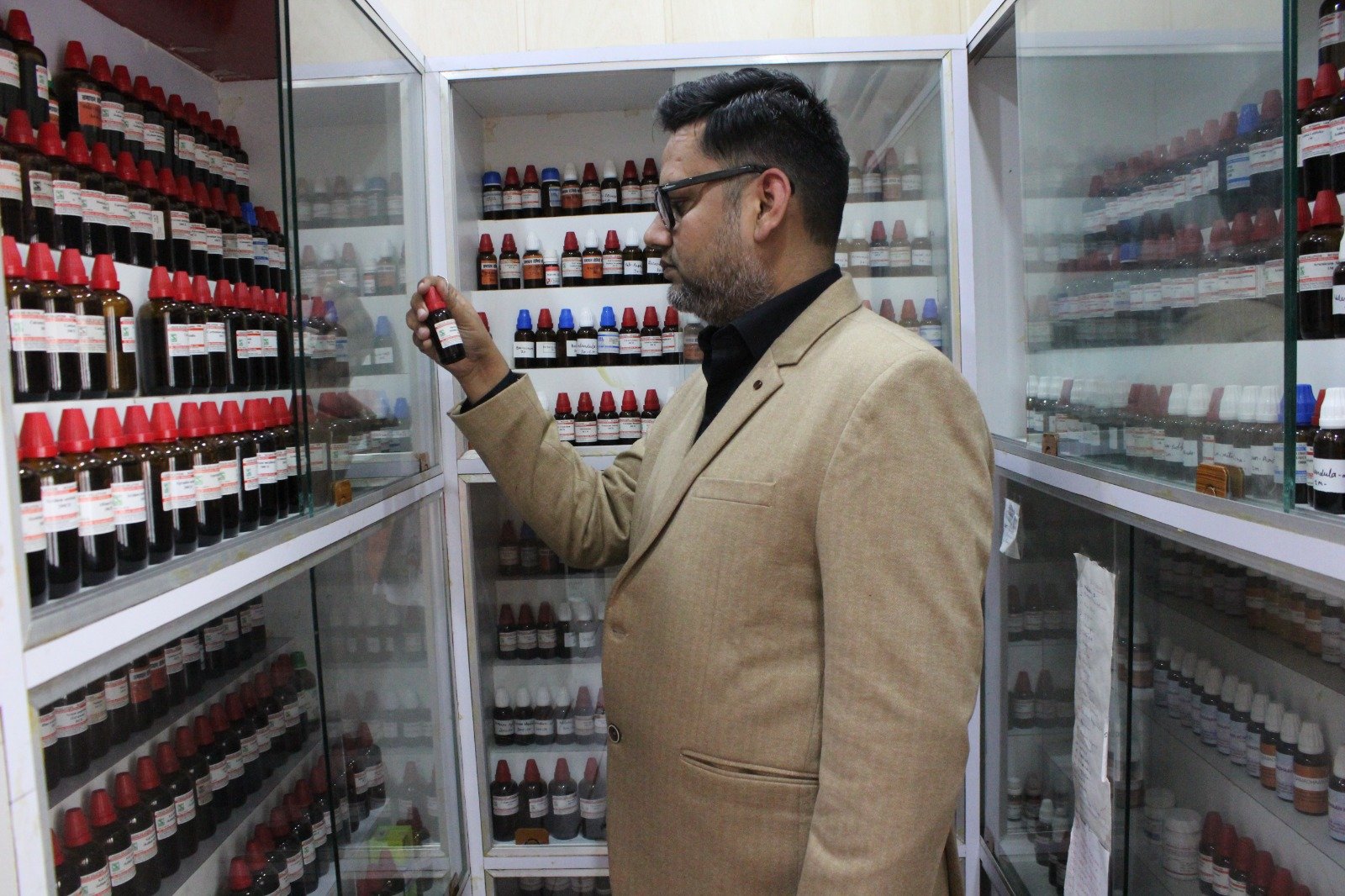 Homeopathic doctor examining medicine bottles in the pharmacy at Samadhaan Homoeo Clinic